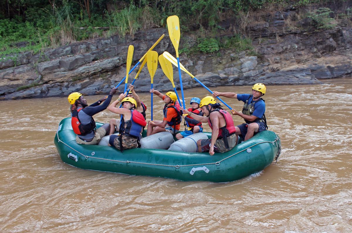 A group of people in a raft riding down a fast-flowing river in Costa Rica's rainforest surrounded by lush greenery